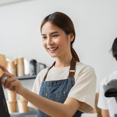 Happy,Young,Asian,Woman,Cashier,Wears,An,Apron,And,Using